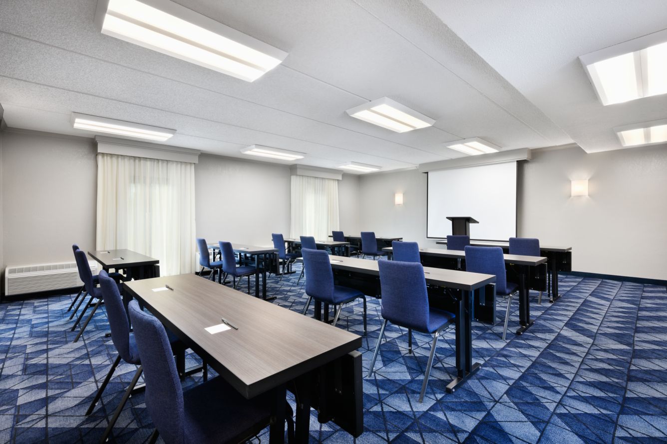 Meeting room set up classroom-style with tables, chairs, and a projector screen