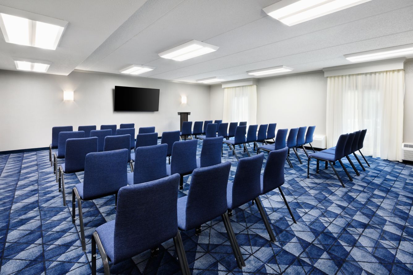 Meeting room set up theater-style with rows of blue chairs facing a wall-mounted TV