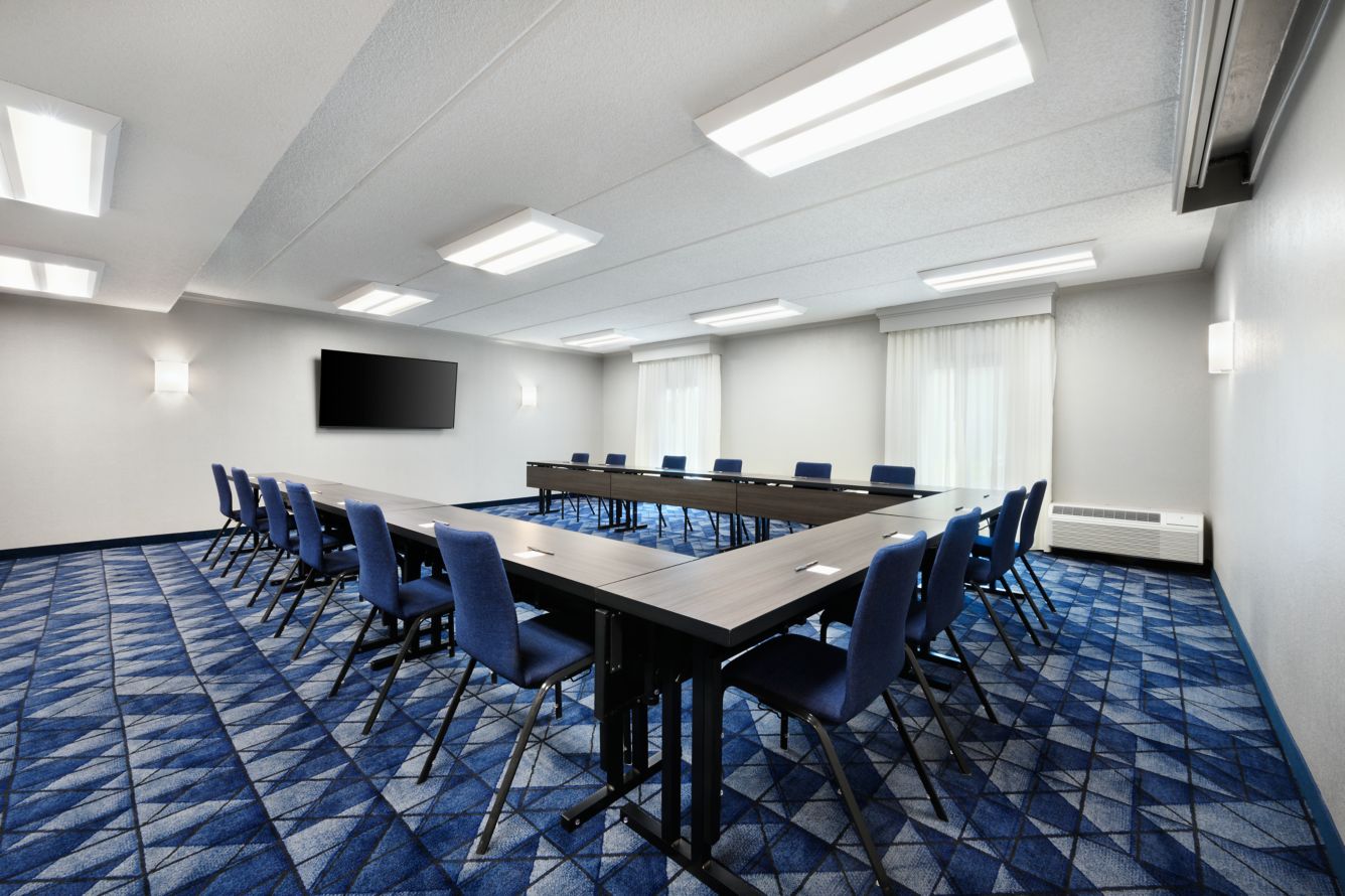 Meeting room set up in a U-shape with tables and blue chairs around a TV